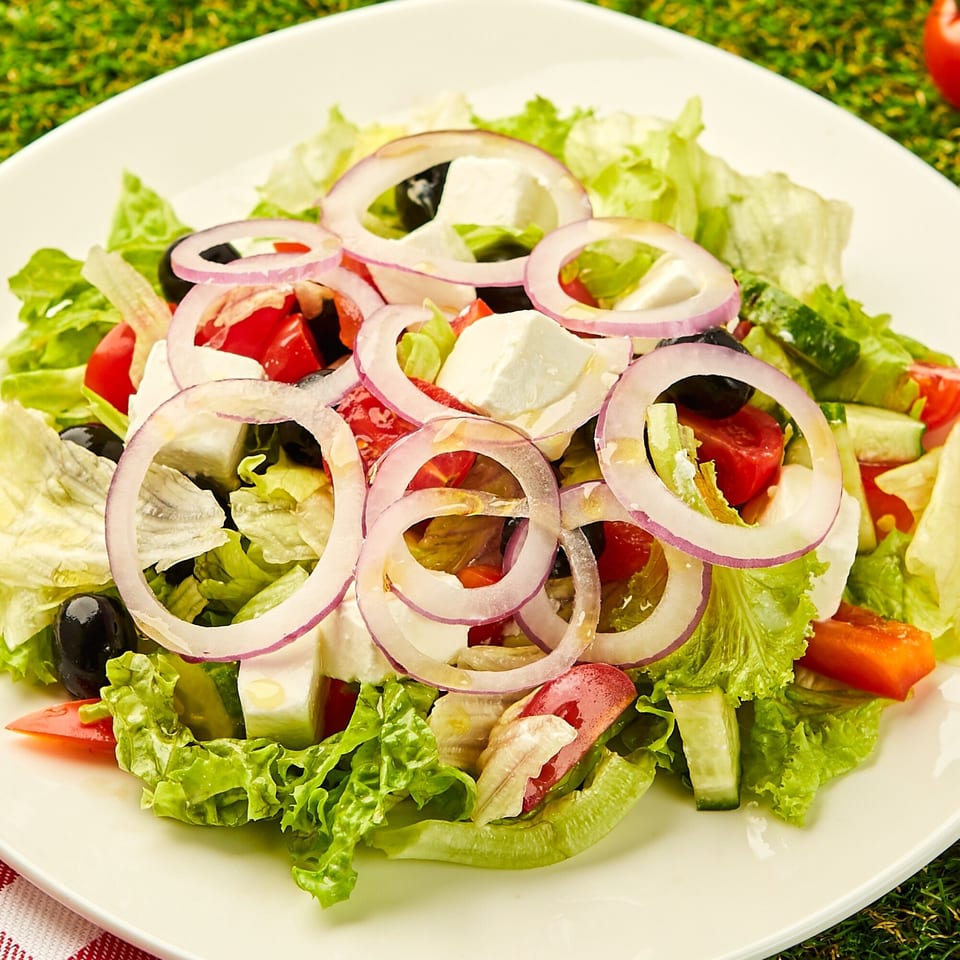 A fresh Bacio Pizza salad with lettuce, tomatoes, cucumbers, feta cheese, black olives, and red onion rings.