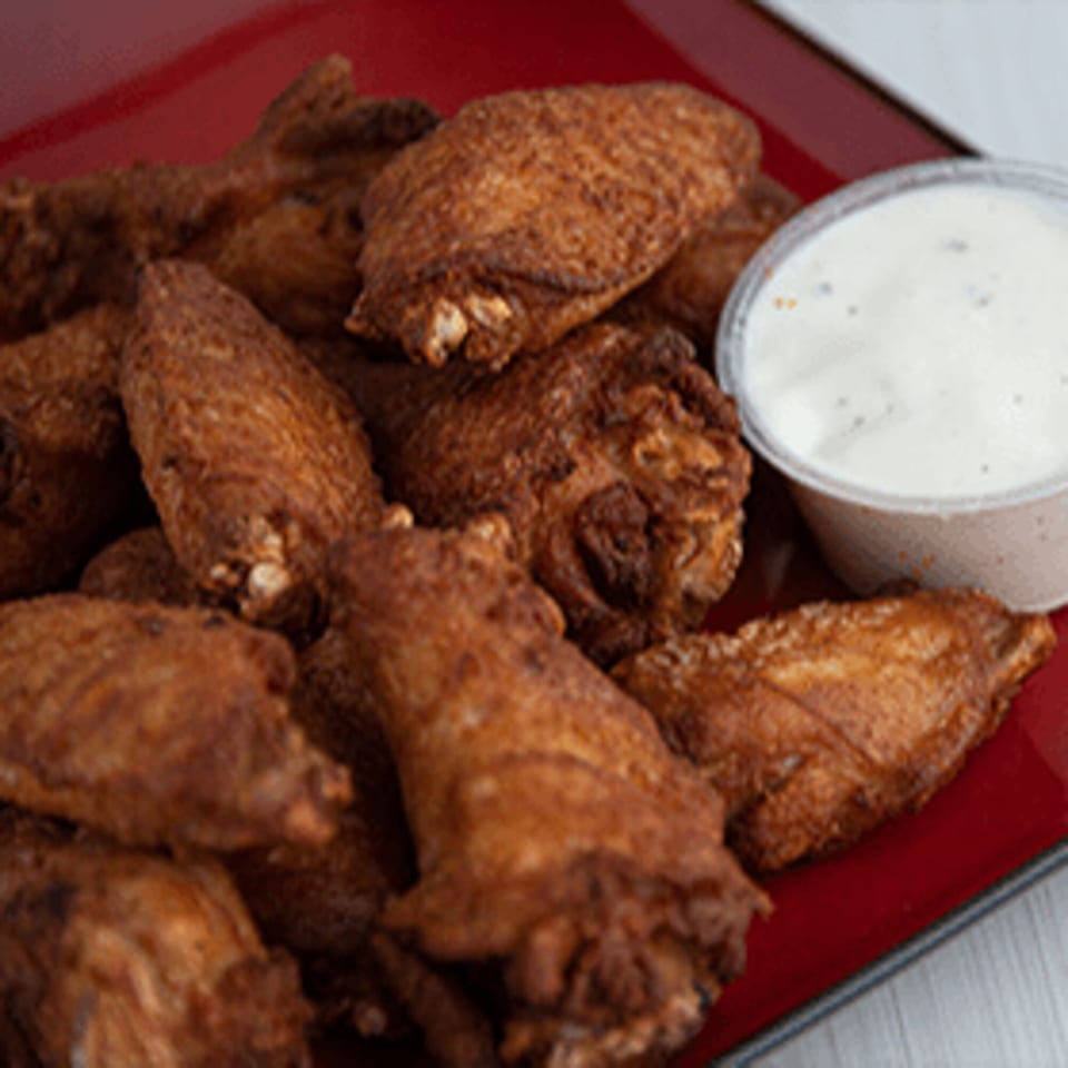 Crispy fried chicken wings on a red plate with a side of ranch dressing from Bacio Pizza.