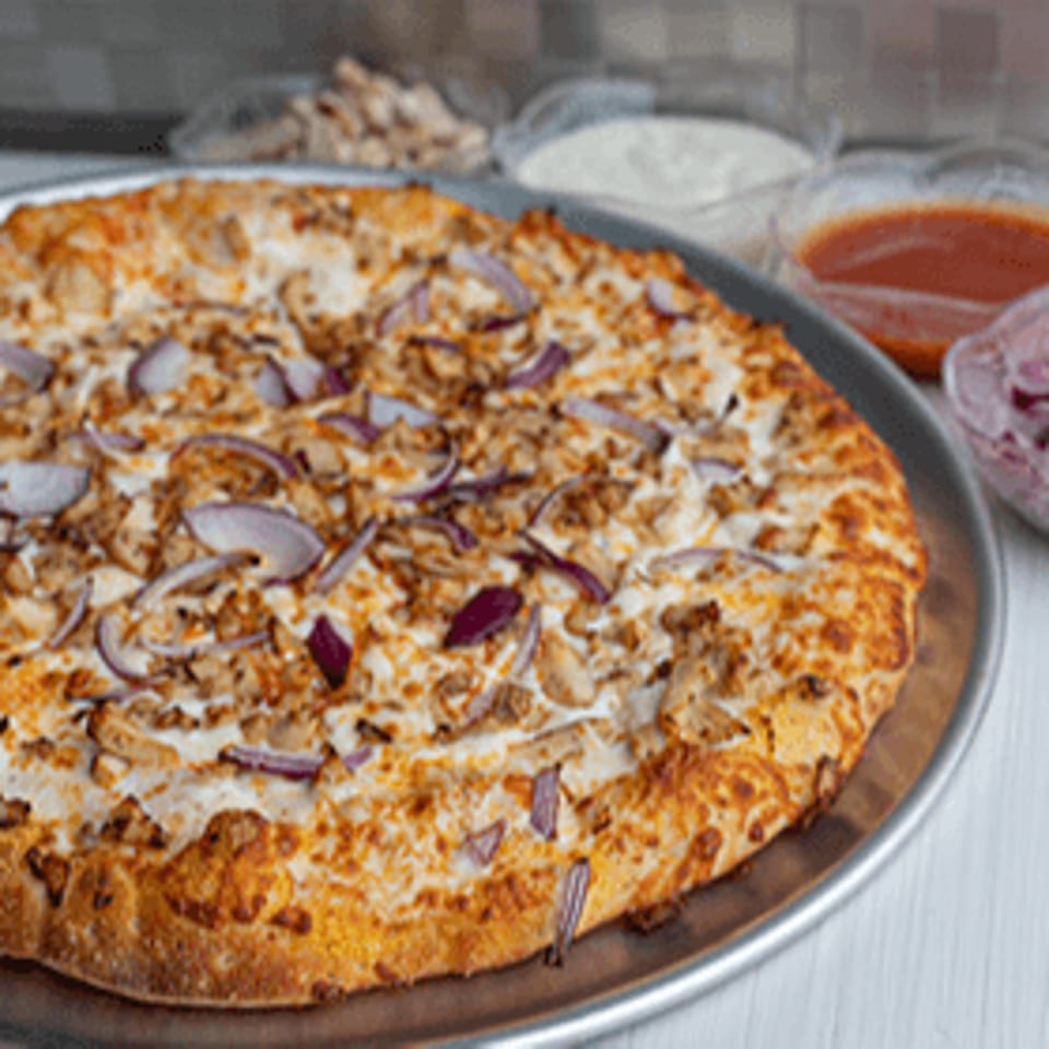 Bacio Pizza's chicken and red onion pizza on a metal tray with dipping sauces in the background.