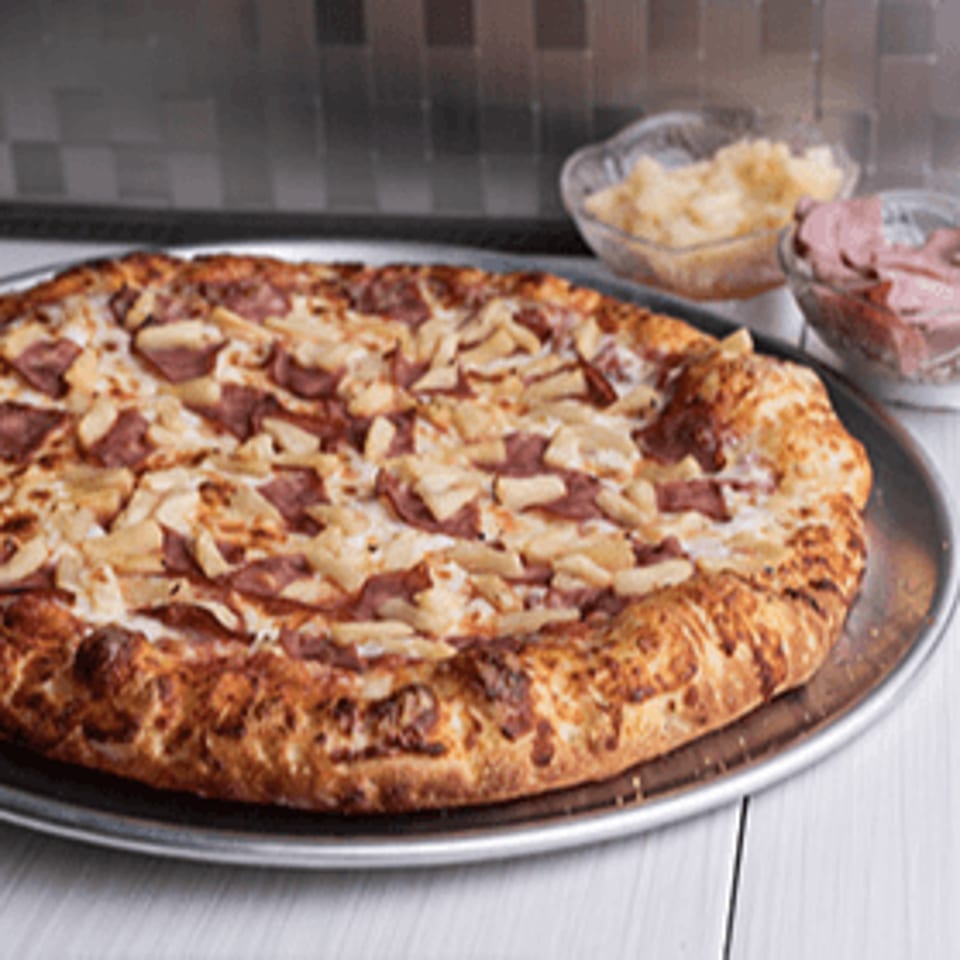 Bacio Pizza's Hawaiian pizza, topped with ham and pineapple, on a metal tray with ingredients in bowls.